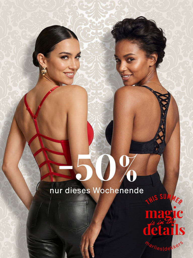 Two women models shown from the back wearing strappy back lingerie from marlies dekkers, one in red and one in black, against a light damask wallpaper background with a text '-50% nur dieses Wochenende'. 'magic to the details' branding.