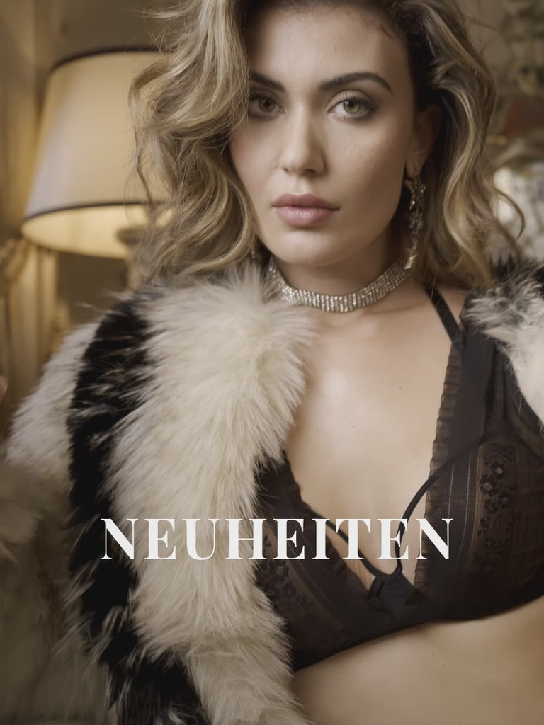 Video of a model with shoulder-length brunette hair wearing a black floral lace lingerie set from marlies|dekkers. She turns to show the bra and matching briefs from the front, side, and back, highlighting the fit and intricate lace details. The word 'neuheiten' appears as an on-screen text overlay.