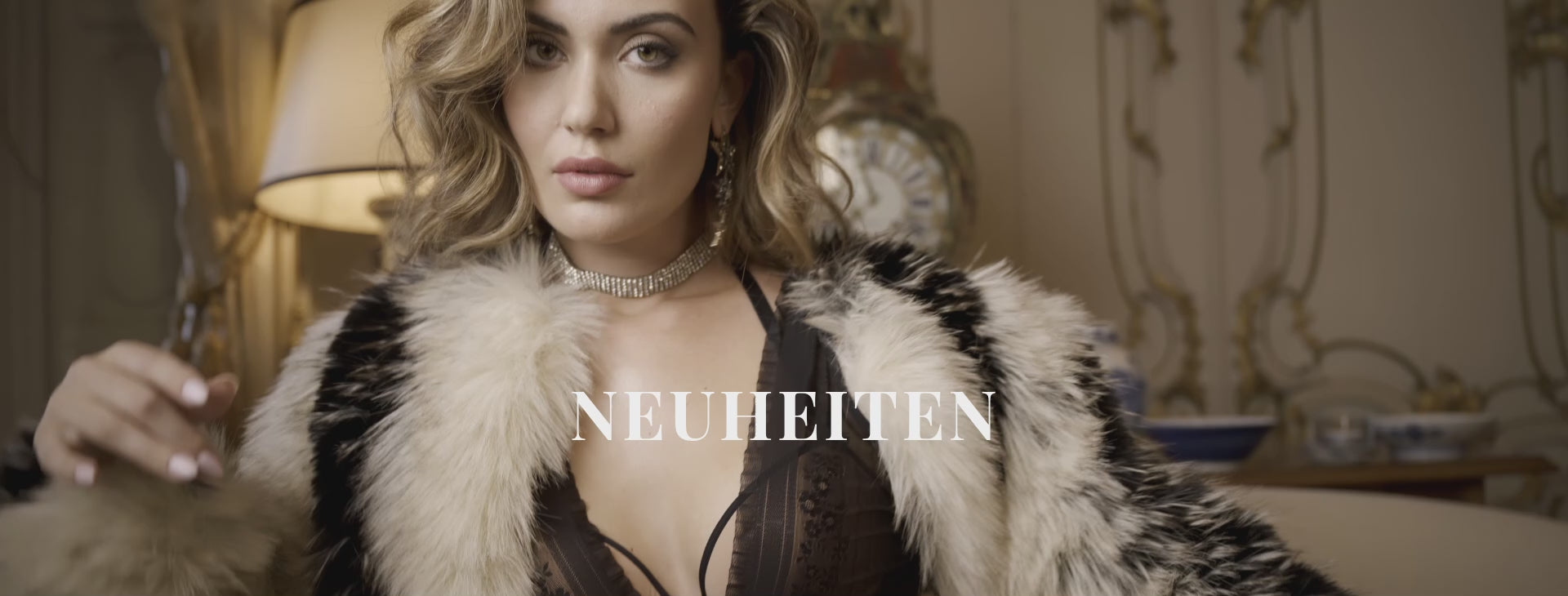 Video of a model with shoulder-length brunette hair wearing a black floral lace lingerie set from marlies|dekkers. She turns to show the bra and matching briefs from the front, side, and back, highlighting the fit and intricate lace details. The word 'Neuheiten' appears as an on-screen text overlay.